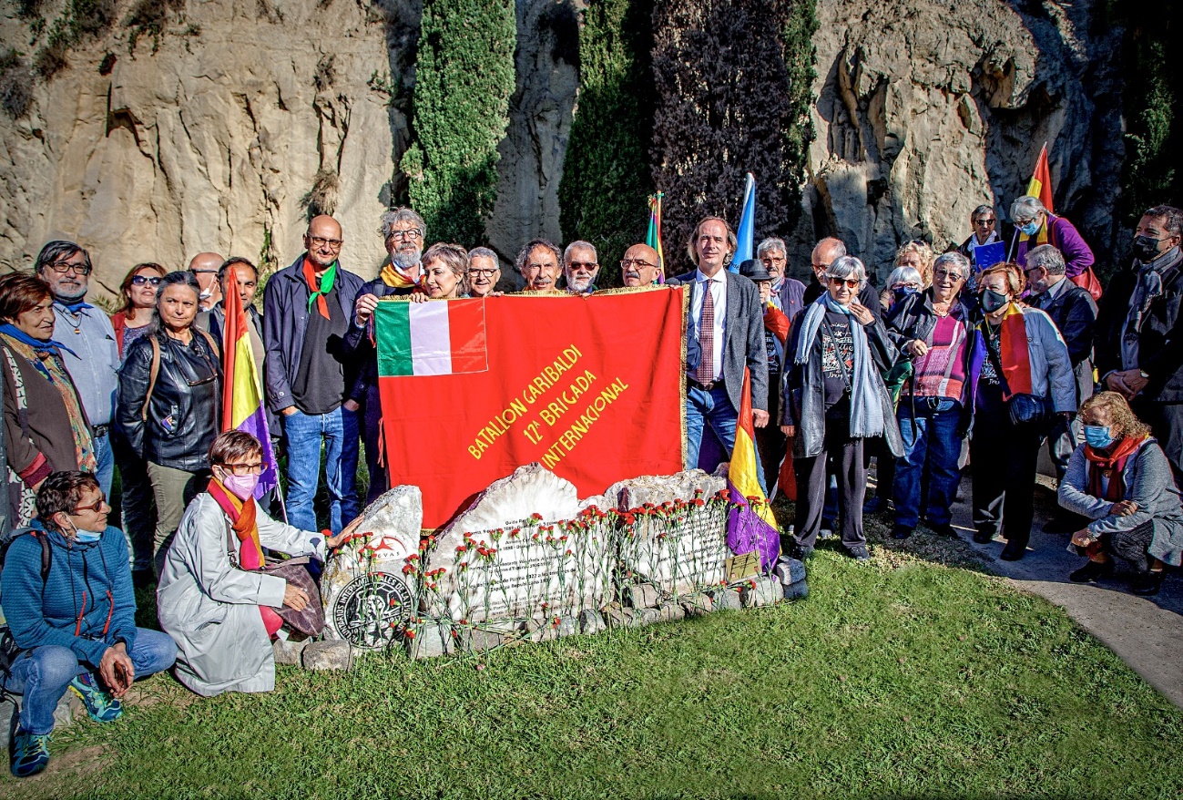 Grup de gent amb les pedres d'homenatge i una bandera del batallón Garibaldi.